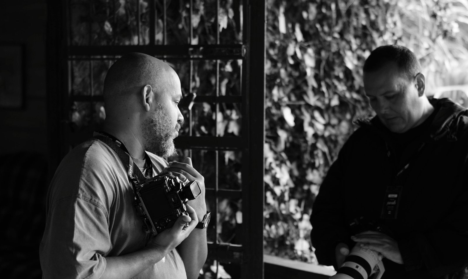 Dramatic black and white image of two photographers engaged with cameras outdoors.